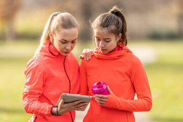 A young female trainer and a junior are checking her sports performance on a tablet
