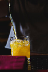 Bright tropical gold cocktail pouring into rocks glass on bar top