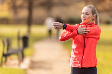 Young woman warming up before jogging, doing upper body stretching in the park