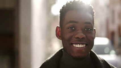 Confident young black man portrait smiling at camera in city during drizzle and sunlight