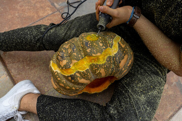young man with a drill or dremel drilling a pumpkin for halloween