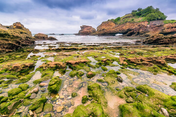 Scenic view of shoreline with rocks and shallow water at Biarritz, France against dramatic storm sky