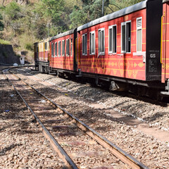 Obraz premium Toy Train moving on mountain slopes, beautiful view, one side mountain, one side valley moving on railway to the hill, among green natural forest. Toy train from Kalka to Shimla in India, Indian Train