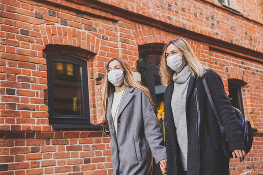 Young pretty girls friends in medical masks having fun outdoor in autumn evening in city laughing and going crazy - end of pandemic concept