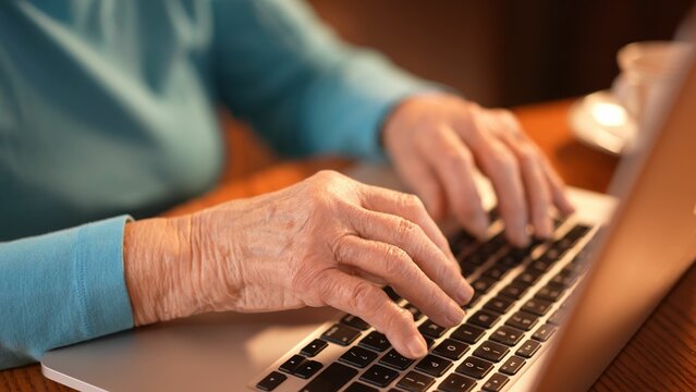 Closeup of elderly womans hands while she types on laptop computer keyboard.