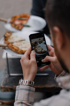 Man takes a photo of eating pizza on his phone during a date with a girl