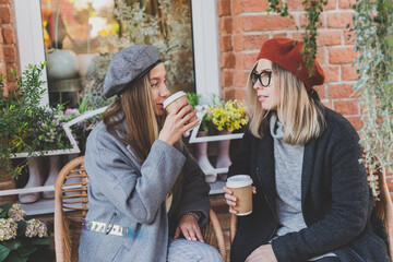 Young female best friends talking to each other discussing interesting themes during free time hipster girls joking and having fun together enjoying recreation with coffee to go on urban background - obrazy, fototapety, plakaty
