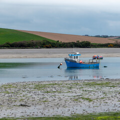 An boat in shallow water at low tide on a cloudy day. Hills under a cloudy sky. Silt and seaweed. Landscape.