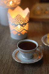 Plate with peanut butter cookies, cup of tea or coffee, open book, reading glasses and lit candles on the table. Selective focus.