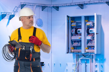 Man is worker at electrical company. Electrical installation specialist. Man with wires near electrical panel. Electrician in helmet stands in engineering room factory. Construction with wire