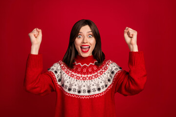 Photo of impressed lucky girl dressed x-mas ornament pullover rising fists screaming isolated red...