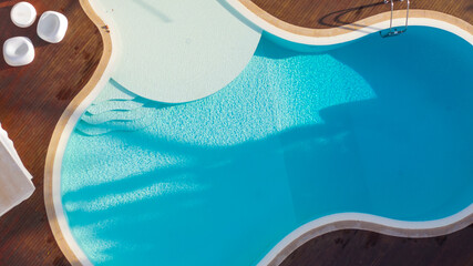 Aerial view of a swimming pool with wavy and curved shapes. Around the pool there is wooden flooring and the garden. Vacation house concept.