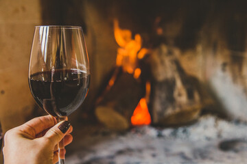 Mão segurando taça de vinho tinto em lareira no inverno