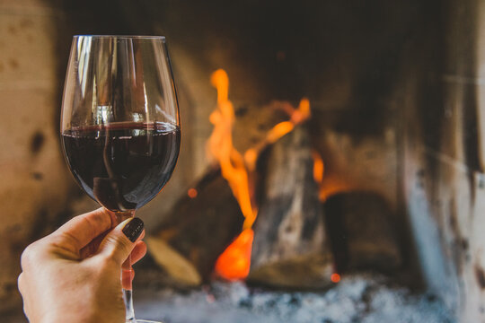 M&atilde;o segurando ta&ccedil;a de vinho tinto em lareira no inverno
