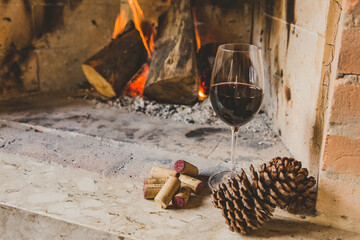 Taça de vinho tinto em lareira no inverno com rolhas e pinhas