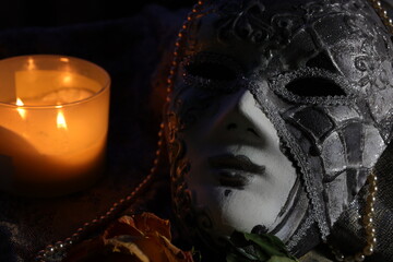 Carnival mask arranged with the burning candle on the black background 