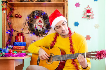 Young handsome man in Santa hat playing guitar and celebrating Christmas