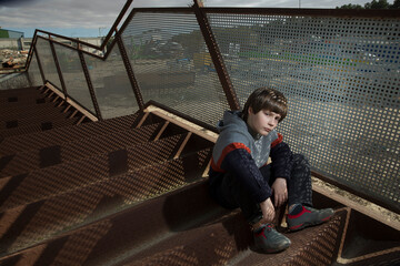 a handsome stylish fair-haired boy poses among colored iron structures in a knitted sweater and...