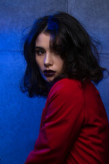 Portrait of woman with makeup and hairstyle, wear red suit, looking at camera sensual, holding hands near face, blue neon studio light.