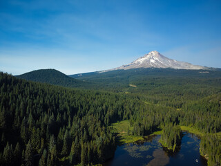 A small dark blue lake, a hilly green meadow and a high mountain covered with snow in the distance, a dormant volcano. Clear cloudless sky. Beautiful nature, ecology.