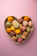 Macaroons colorful cookies in wooden heart bowl. Macarons french sweet dessert, top view, pink background. Copy space