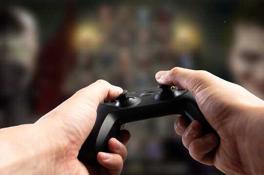 A joystick in the hands of a gamer against the background of a video game on a large screen TV, personal computer. Youth culture, virtual reality, cyberspace, online games.