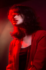 Profile portrait of young woman with makeup and hairstyle, wear red suit, with closed eyes, red neon studio light. Vertical view.