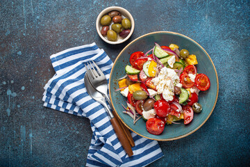 Greek fresh healthy colorful salad with feta cheese, vegetables, olives in blue ceramic bowl on...