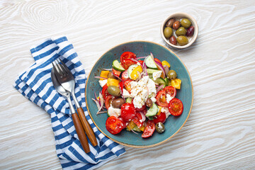 Greek fresh healthy colorful salad with feta cheese, vegetables, olives in blue ceramic bowl on rustic white wooden background top view, Mediterranean diet, traditional cuisine of Greece 