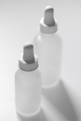 Close-up of two different-sized empty white translucent glass dropper vials, one bottle in front and in focus. Vertical beauty and lifestyle background, mockup, and copy space on white surface.