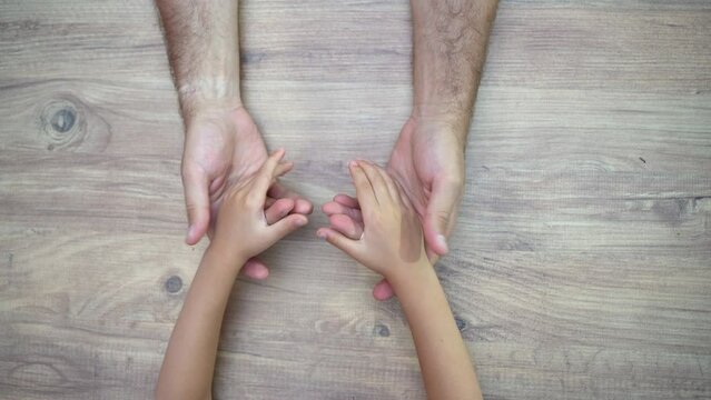 Father and child hands over wooden table, playing, having fun. Topside view