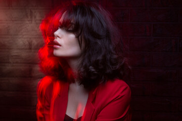 Closeup portrait of a young woman with makeup and hairstyle, wear red suit, with closed eyes, red studio light and effects.