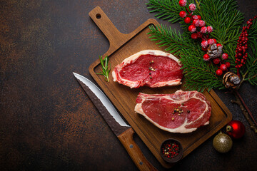 Two raw uncooked meat beef steaks on wooden cutting board with knife and seasonings on dark rustic...
