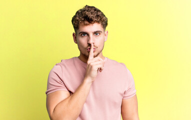 young adult caucasian man looking serious and cross with finger pressed to lips demanding silence...