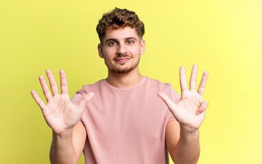 young adult caucasian man smiling and looking friendly, showing number nine or ninth with hand...