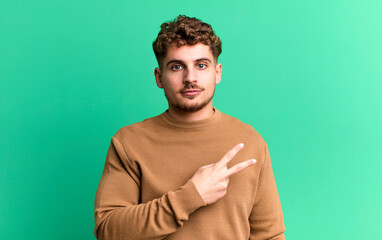 young adult caucasian man feeling happy, positive and successful, with hand making v shape over chest, showing victory or peace