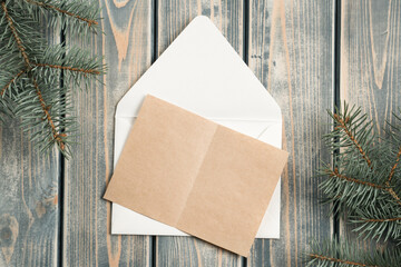 White open Christmas envelope on gray wooden background with blank kraft paper greeting card. Copy space. Top view