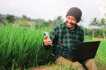 Indonesian young man working Remotely at the middle of Rice Fields.