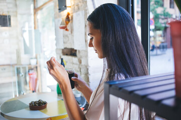 Side view of contemplative Caucasian woman holding glass of cold coke and thinking during daytime...