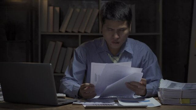 Businessman stressed with working overtime with a desktop computer and picking up documents that haven't been free until late at the office. business people work overtime salaryman concept