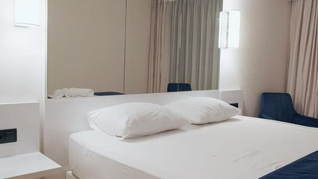 Large queen size bed in modern city hotel room for business trips. Ascetic, minimalistic interior with everything you need to relax after work. Electrical outlets for charging devices.