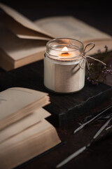 Selective focus burning soy candles in a glass jar with a wooden lid on table with books. Place for a label. Wax and wick. Home decor. Handmade. Air freshener. 