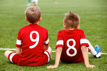 Two young boys as a teammates in sports team sitting on pitch sideline. Friendship in junior sport....