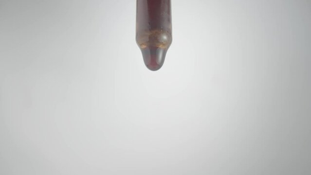 Drop Of Brown Liquid, Oil, Serum Or Tincture Dripping From Pipette On A Gray Background. Macro Shot Of Dripping Drops Of Iodine Or Essential Oil. Concept Of Medicine, Health, Treatment. Aroma, Herbal