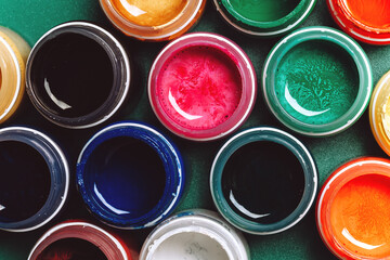 Beautiful, bright, mother-of-pearl, multicolored open cans of paint on a green background. View from above. The concept of creativity.