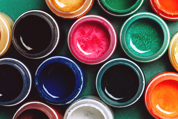 Fototapeta premium Beautiful, bright, mother-of-pearl, multicolored open cans of paint on a green background. View from above. The concept of creativity.