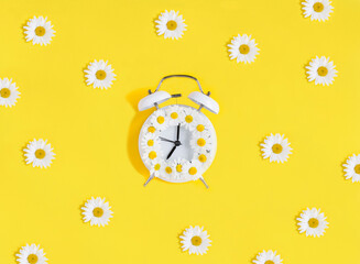 White chamomile and alarm clock on the yellow background. Close-up. Flat lay.