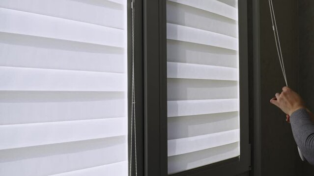 a woman opens the fabric roller blinds with day-night effect on window.