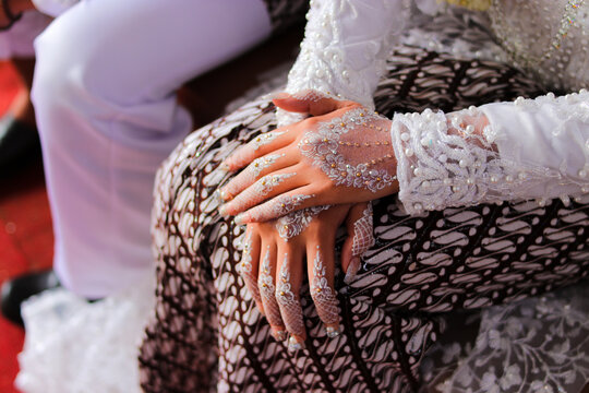 Traditional Sundanese Bride with white nail art and white kebaya dress sitting beside her husband on the wedding aisle