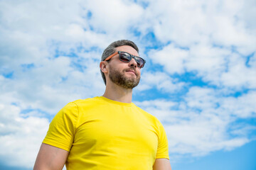 unshaven man wearing yellow shirt and sunglasses outdoor on sky background